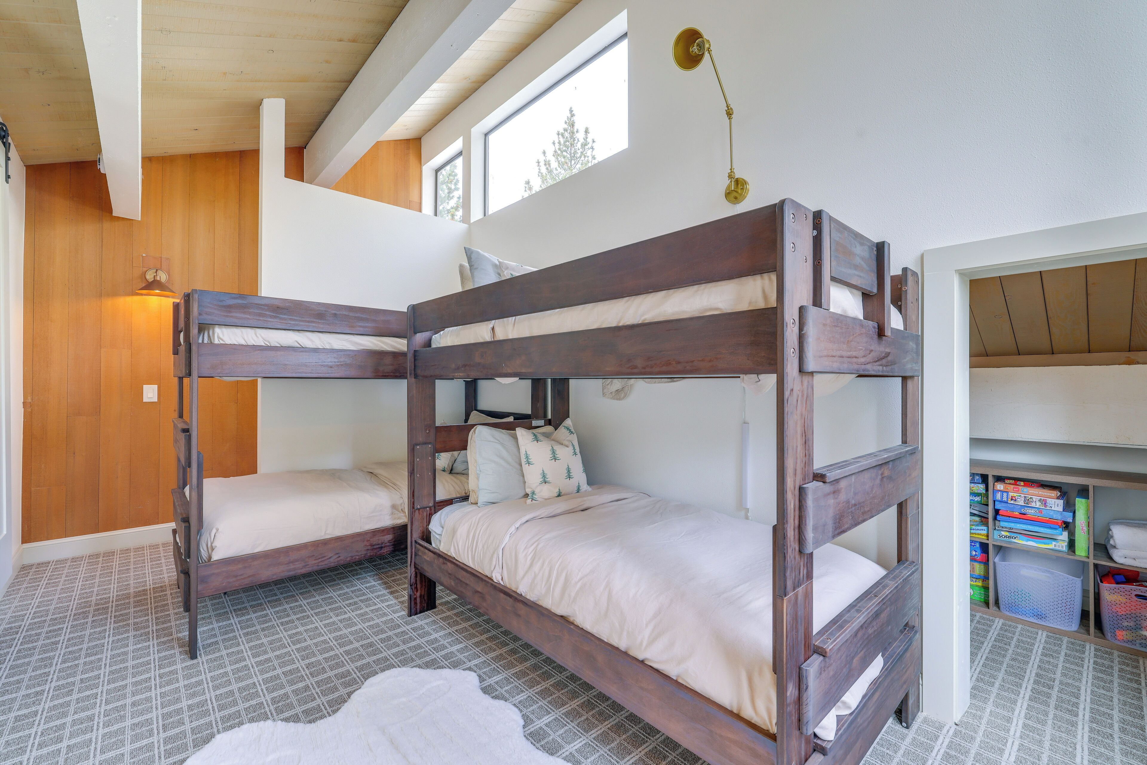 Habitación con literas, techo de madera, una ventana pequeña y una estantería con libros y cajas de almacenamiento.
