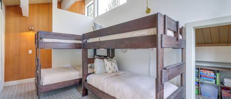Habitación con literas, techo de madera, una ventana pequeña y una estantería con libros y cajas de almacenamiento.