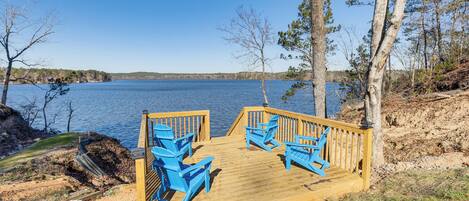 A wooden deck with blue chairs and a wooden railing overlooking a lake.