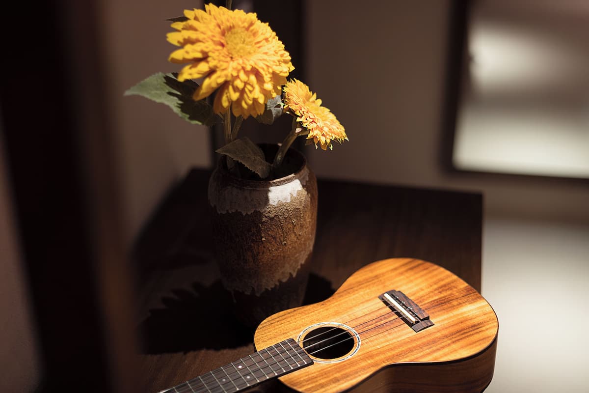 A wooden guitar and a vase with yellow flowers on a wooden surface.
