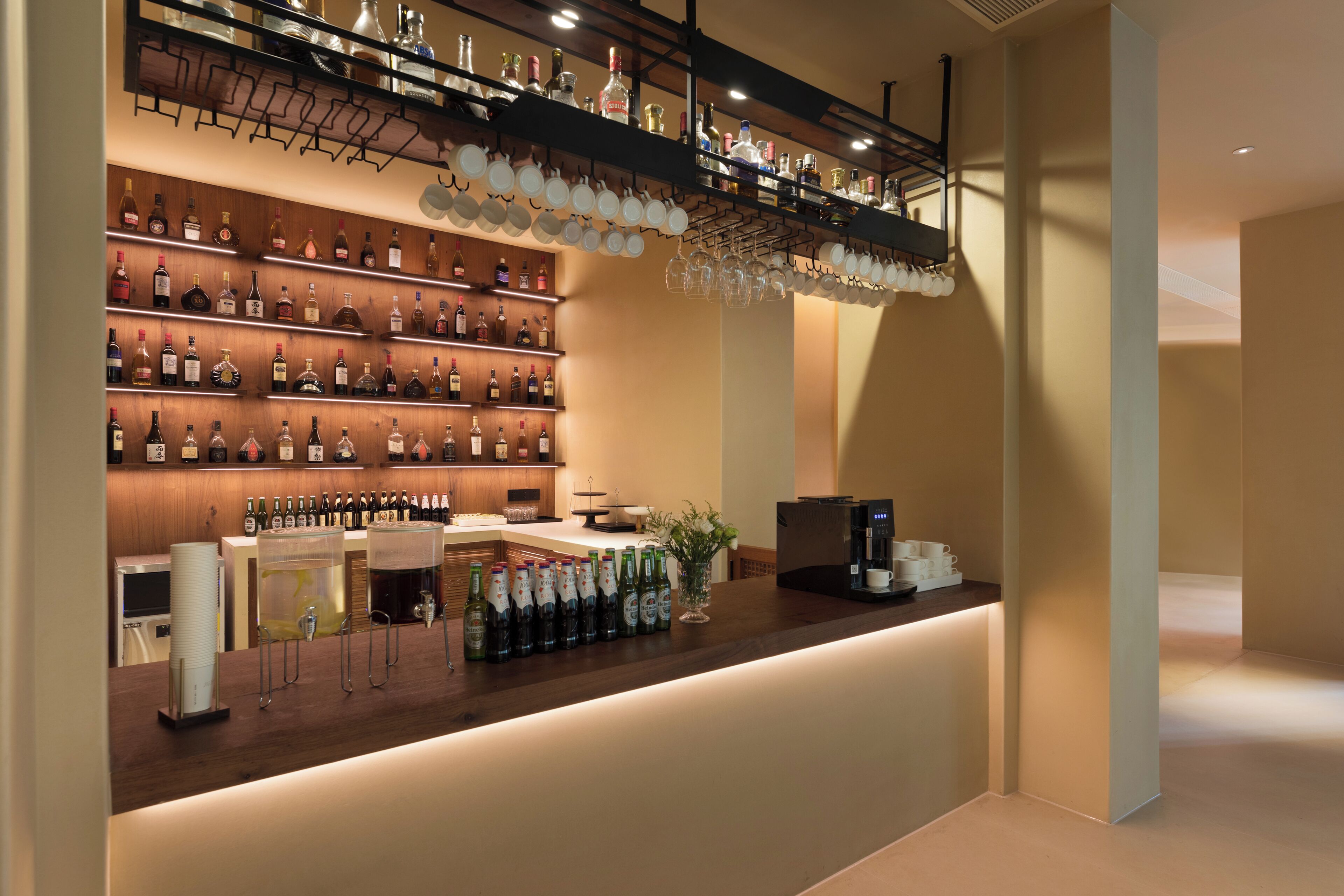 A bar area with shelves of liquor bottles, a coffee machine, and a counter with glasses and bottles.