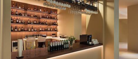 A bar area with shelves of liquor bottles, a coffee machine, and a counter with glasses and bottles.