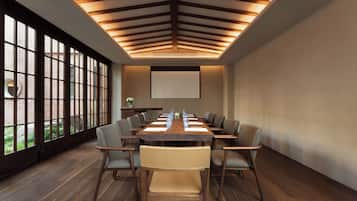 A conference room with a long table, chairs, a projector screen, and large windows with a view of a brick building.