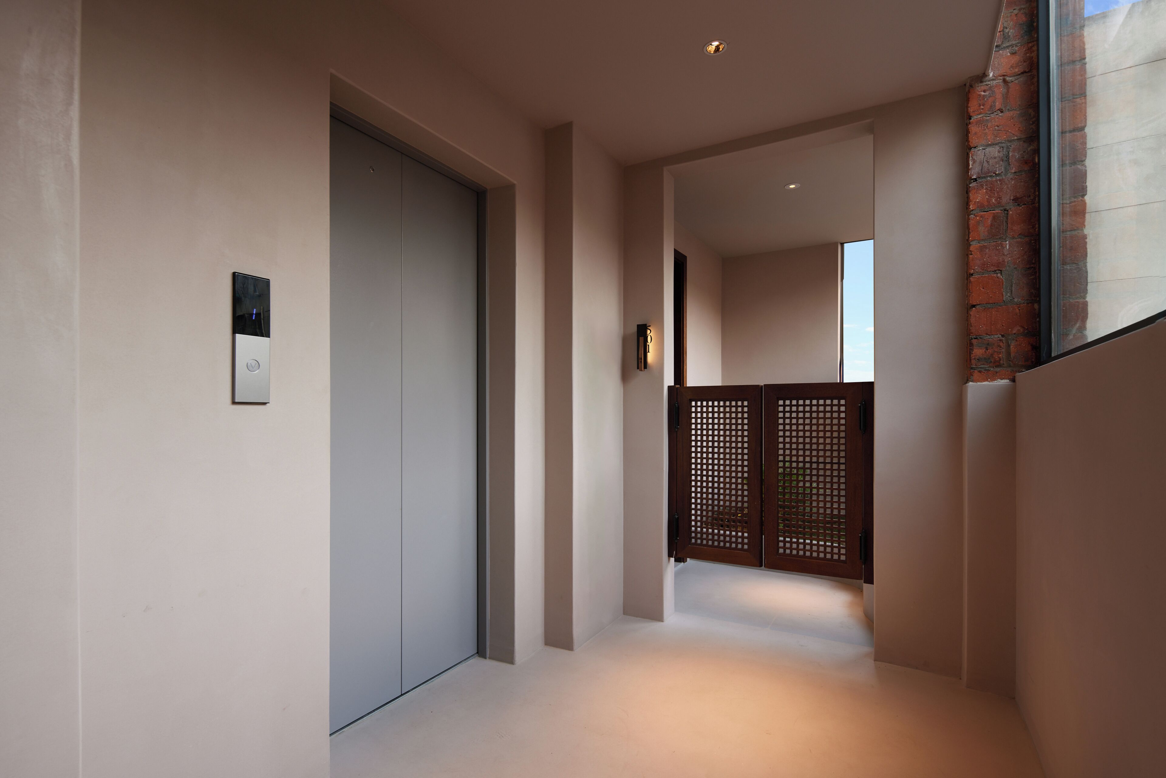 Un couloir moderne avec une porte fermée, un luminaire fixé au mur et une cloison en bois.