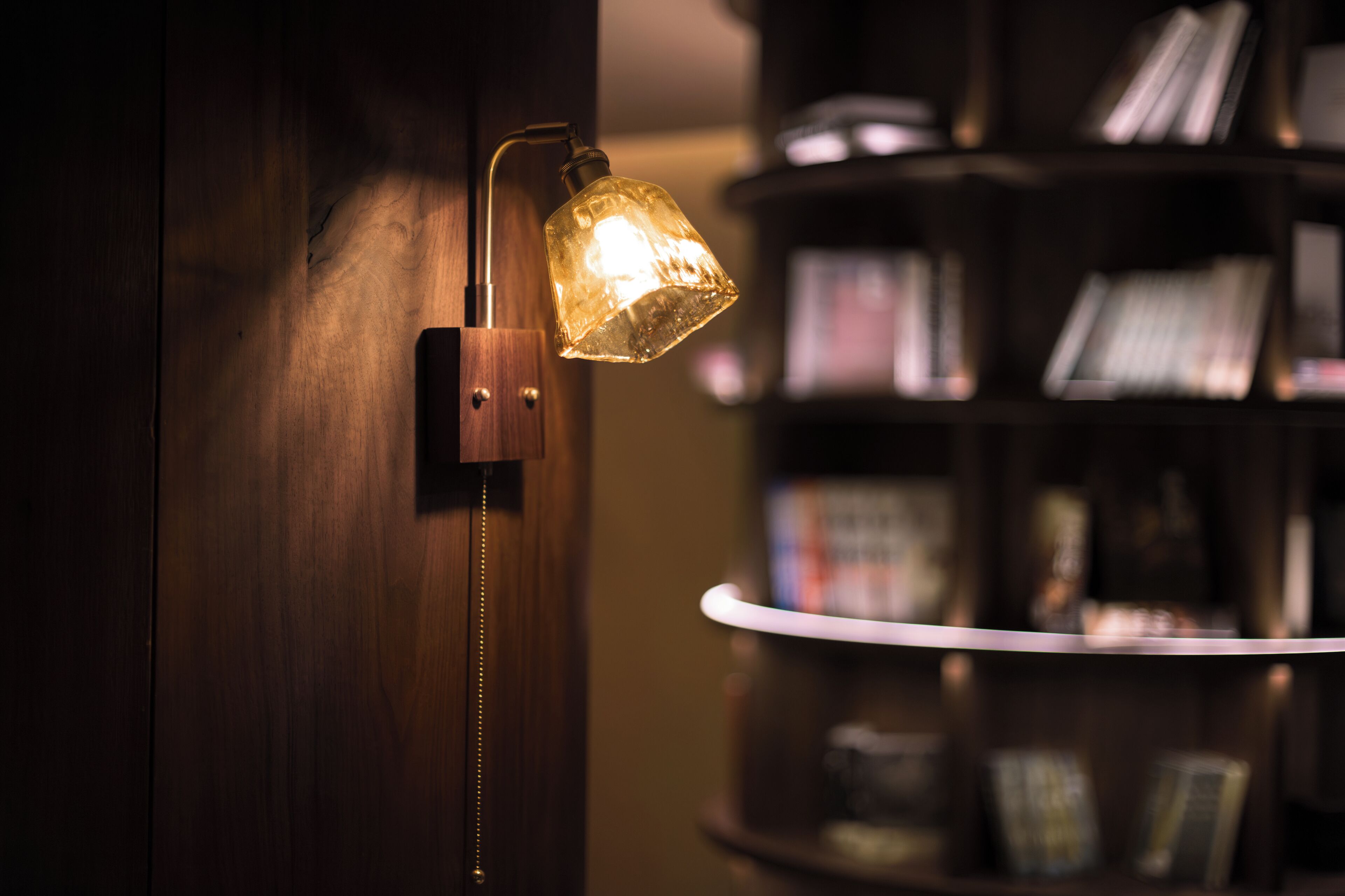 A wall-mounted lamp with a curved design, a wooden door, and a bookshelf in the background.