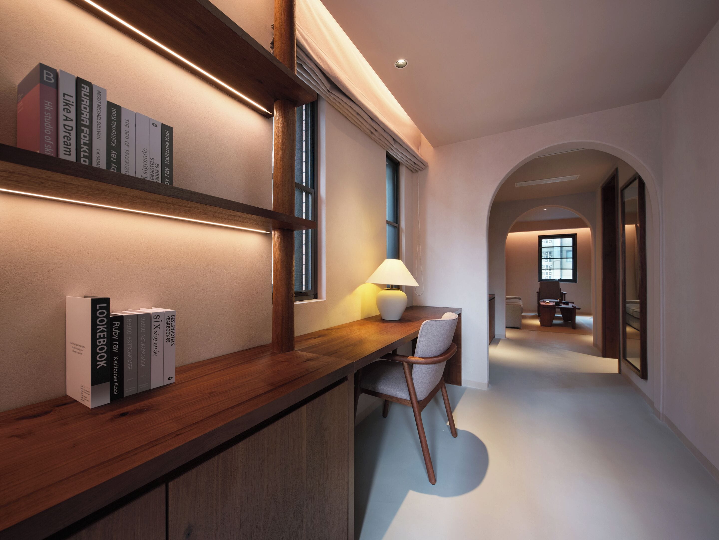 A modern hallway with a wooden desk, bookshelves, and a lamp.
