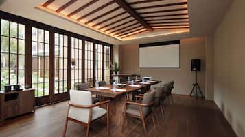 A conference room with a long table, chairs, a projector screen, and a wooden ceiling.
