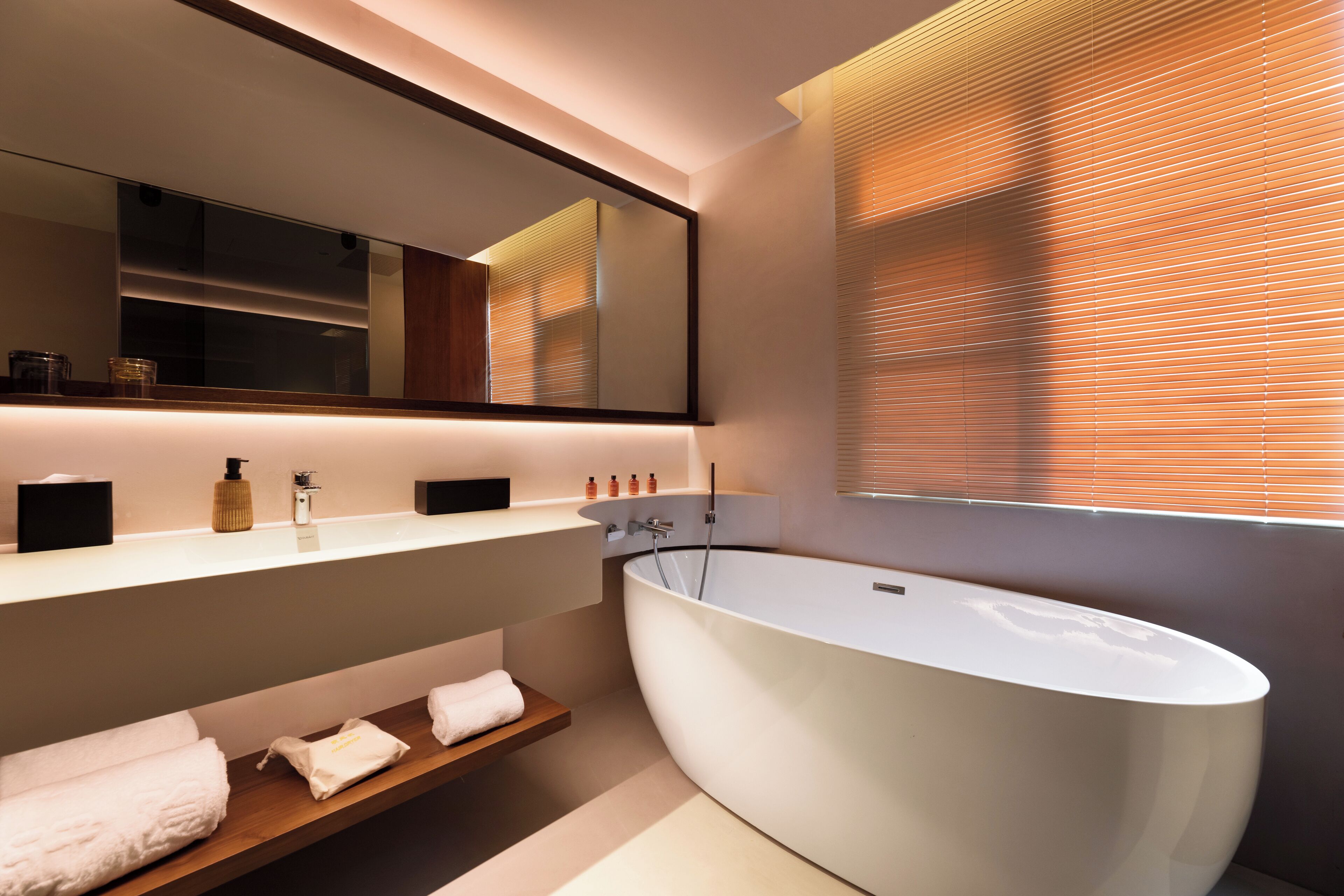A modern bathroom with a freestanding bathtub, a large mirror, and a vanity with a shelf holding towels.
