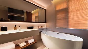 A modern bathroom with a freestanding bathtub, a large mirror, and a vanity with a shelf holding towels.