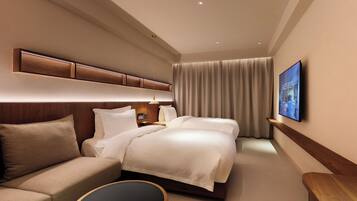 A modern hotel room with a large bed, a sofa, a flat-screen TV, and a wooden headboard.