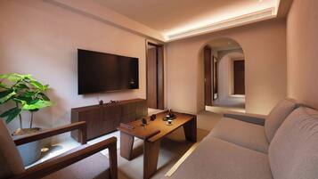 A modern living room with a flat-screen TV, wooden furniture, a large plant, and a sofa.