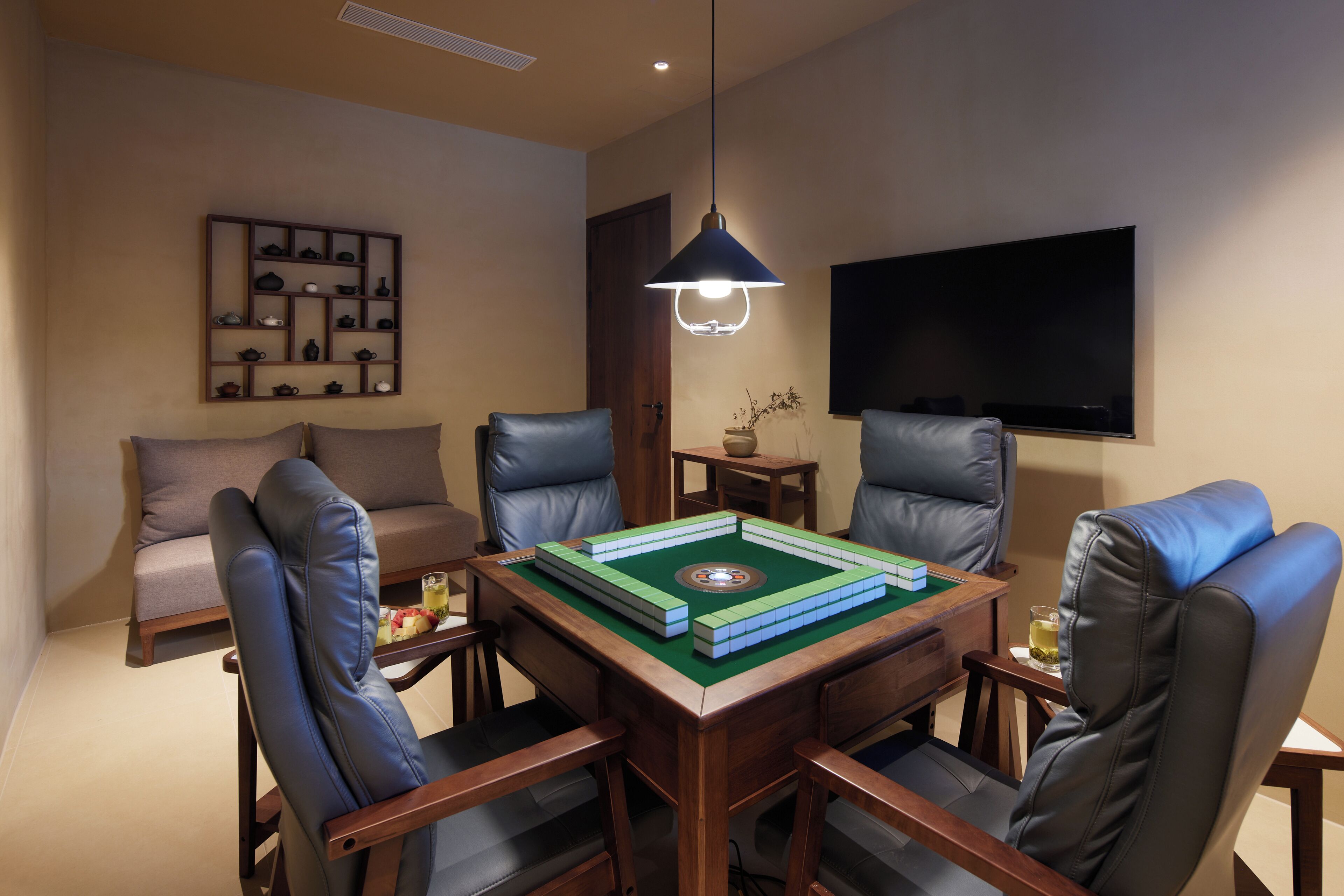 A room with a wooden table, four leather chairs, a bookshelf, a television, and a hanging light fixture.