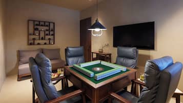 A room with a wooden table, four leather chairs, a bookshelf, a television, and a hanging light fixture.
