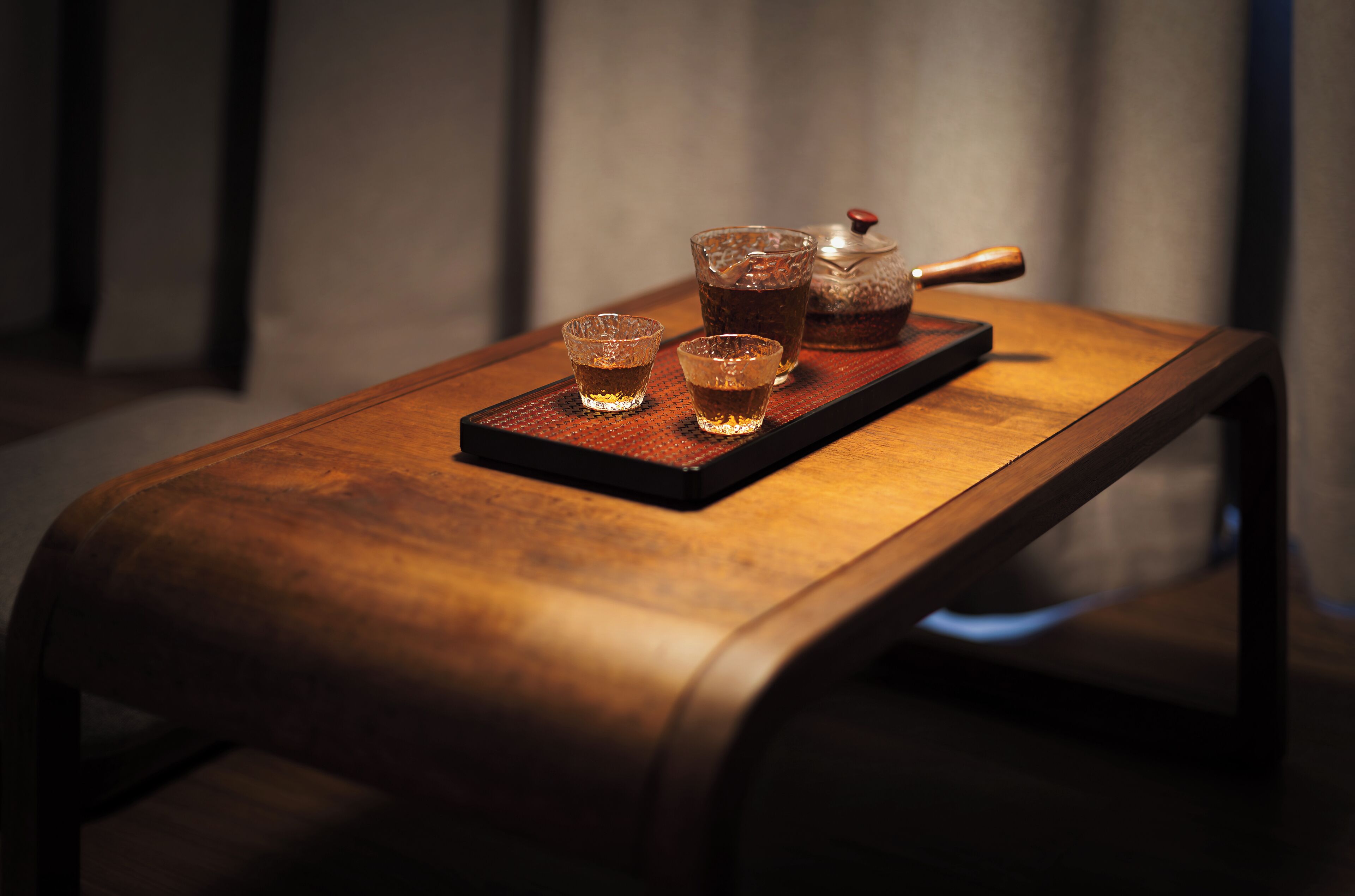 A wooden table with a tray holding a teapot and two cups.