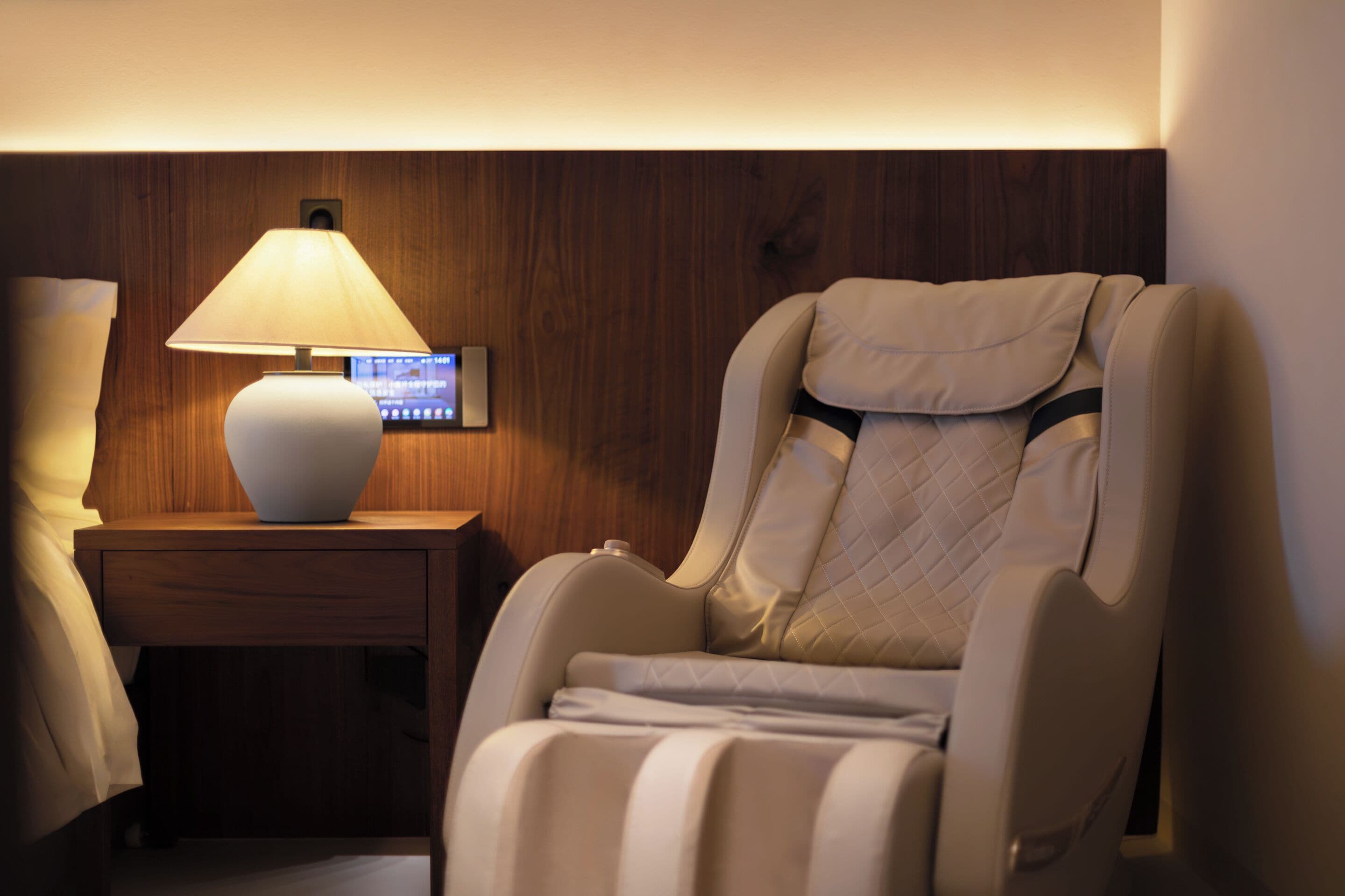 Un fauteuil de massage doté d’un panneau de commande, une table de chevet avec une lampe et un mur en bois.
