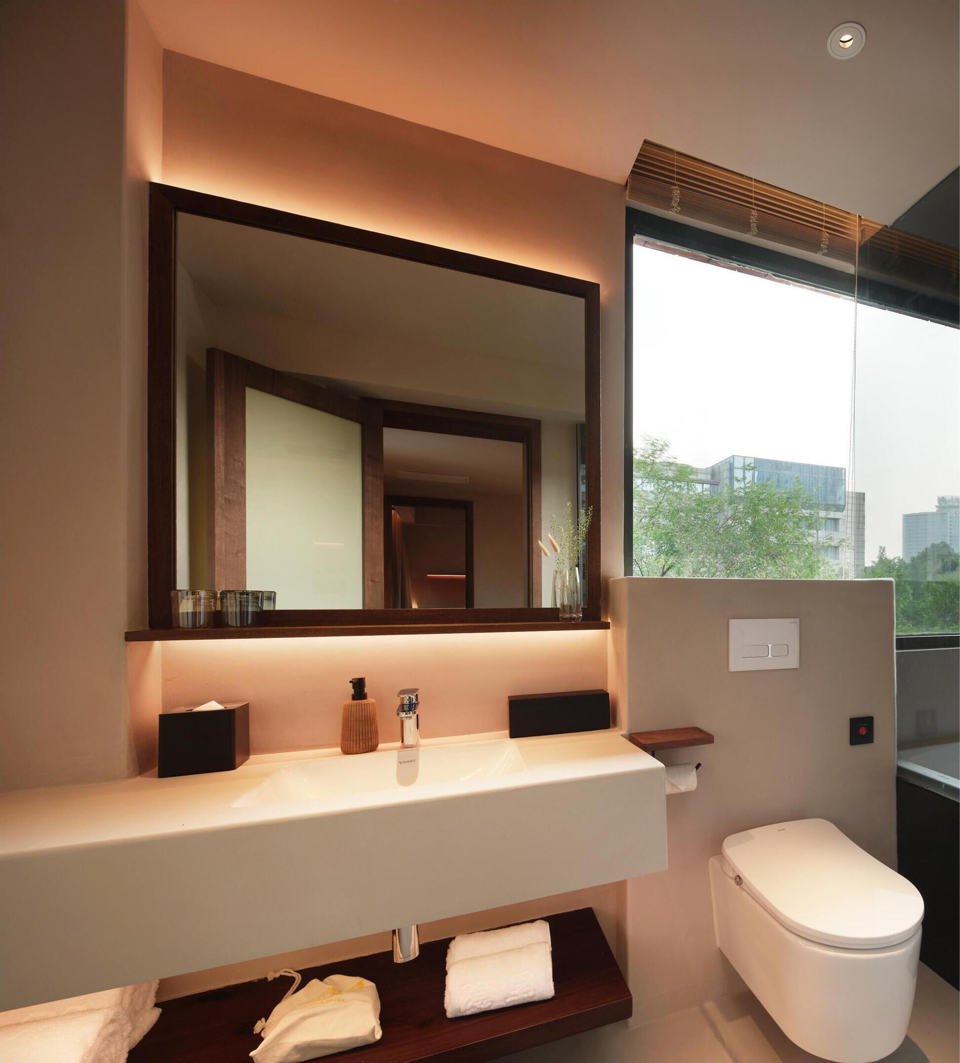 A modern bathroom with a large mirror, a white sink, and a toilet.