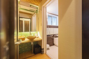 Une salle de bain avec un meuble-lavabo en bois, un grand miroir, un pare-chocs vert à motifs et une fenêtre.