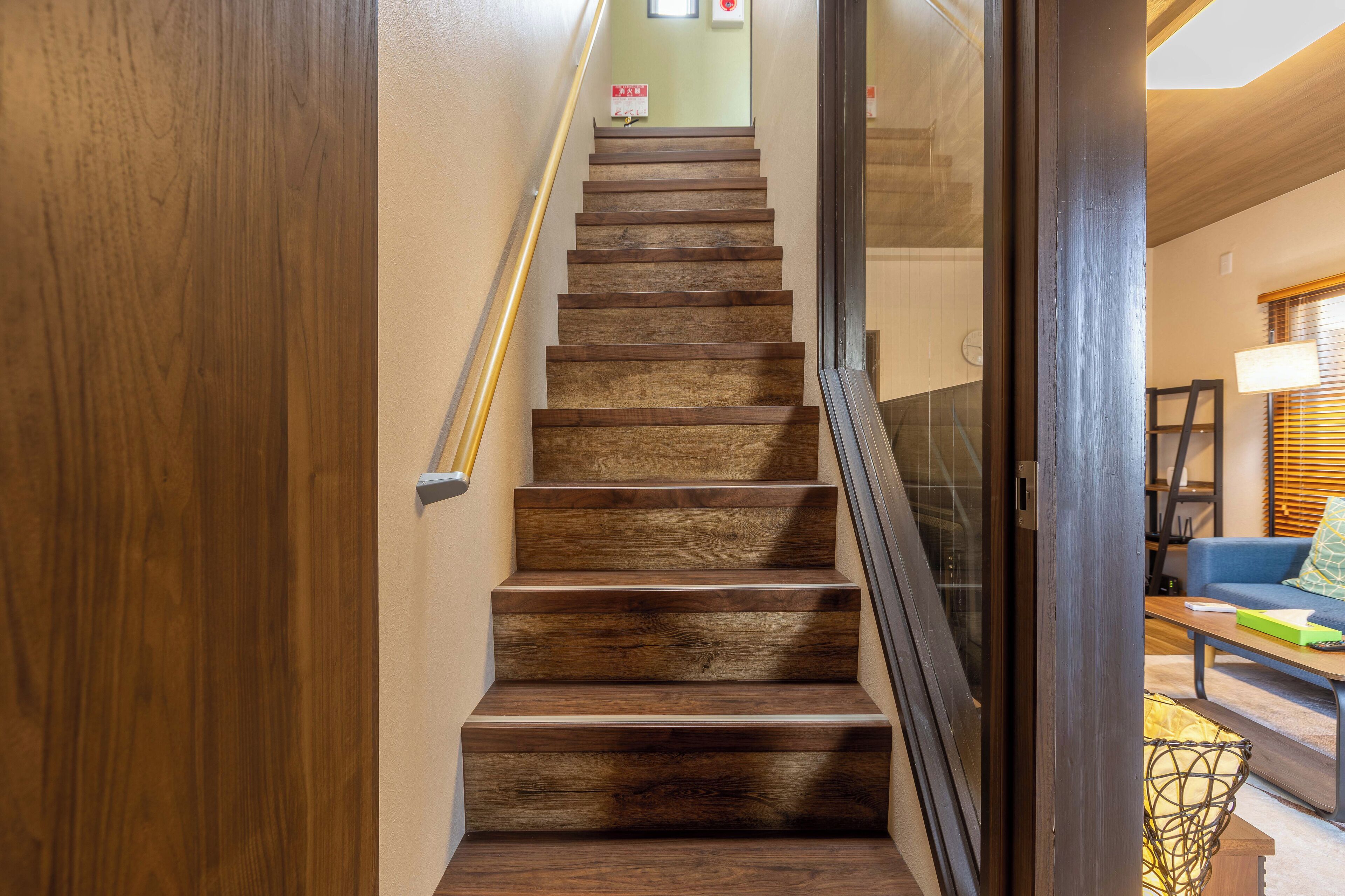 A wooden staircase with a handrail, leading to a room with a blue sofa and a lamp.