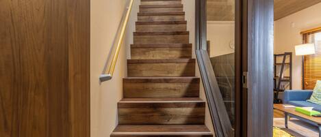 A wooden staircase with a handrail, leading to a room with a blue sofa and a lamp.