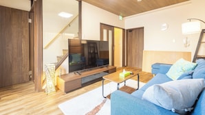 Un salon moderne avec un plancher en bois, un canapé bleu, une table basse, un téléviseur et un escalier.