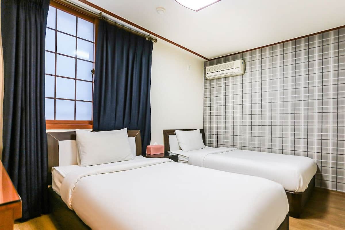 Habitació d'hotel amb dos llits, una finestra amb cortines, un aire condicionat i una paret amb rajoles.