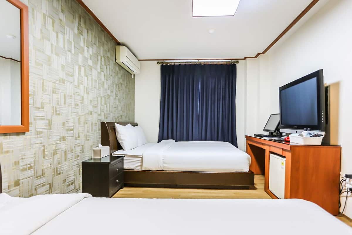 Habitació d'hotel amb un llit, una taula de treball amb un ordinador, una televisió i un frigorífic petit.