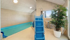 Ett inomhuspoolområde med en blå vattenrutschkana, en sittgrupp och en krukväxt.