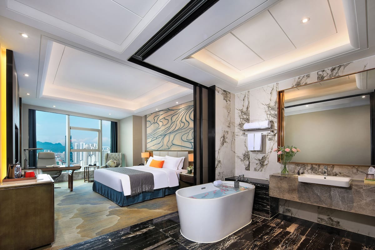 Una habitación de hotel moderna con una cama grande, zona de estar, bañera y baño con encimera y lavabo de mármol.
