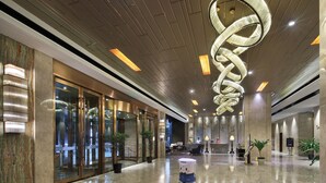 Um saguão moderno de hotel com uma grande luminária espiral, portas de vidro e plantas em vasos.