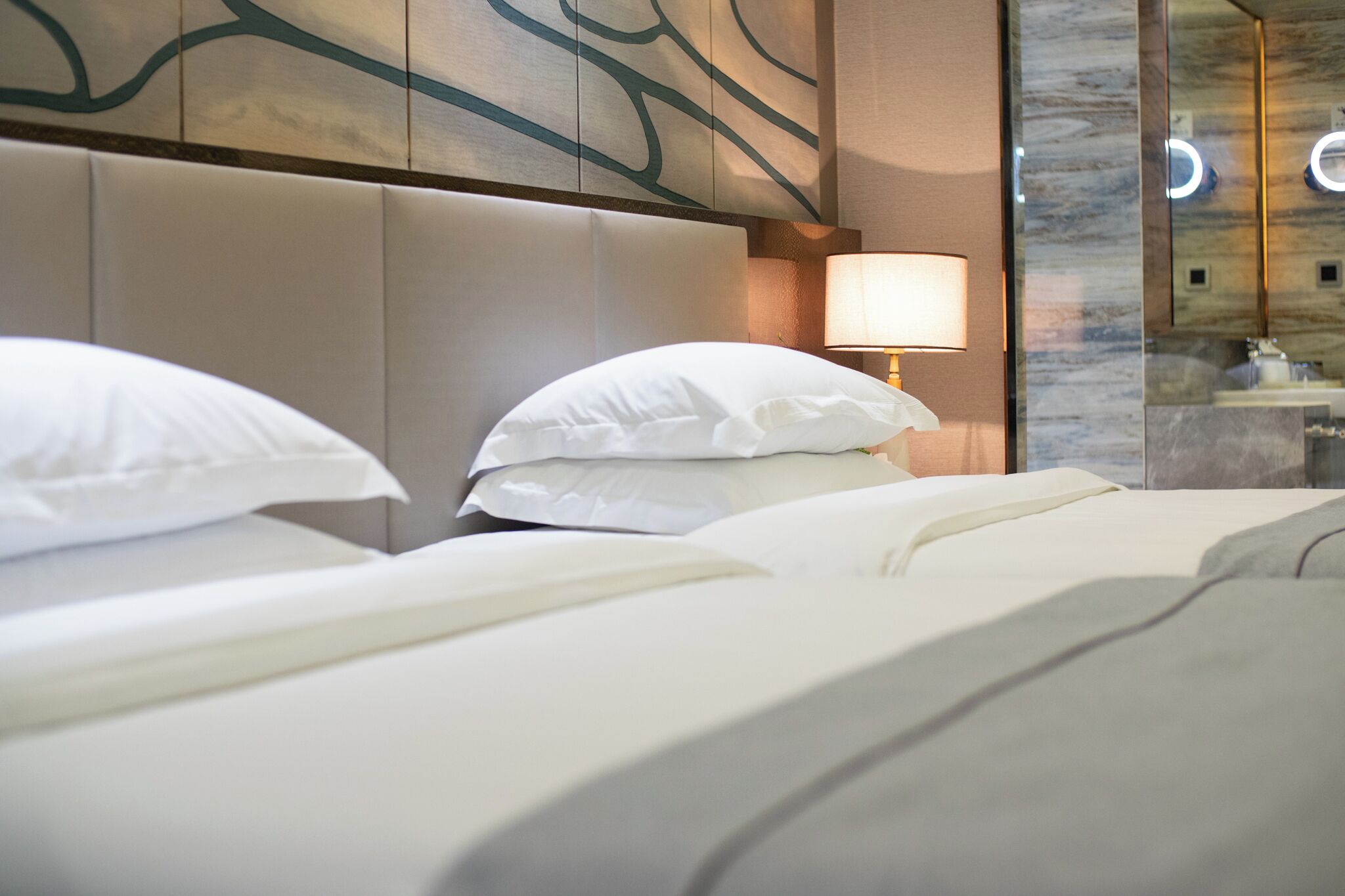 A hotel room with a large bed, a headboard, a bedside lamp, and a mirror.