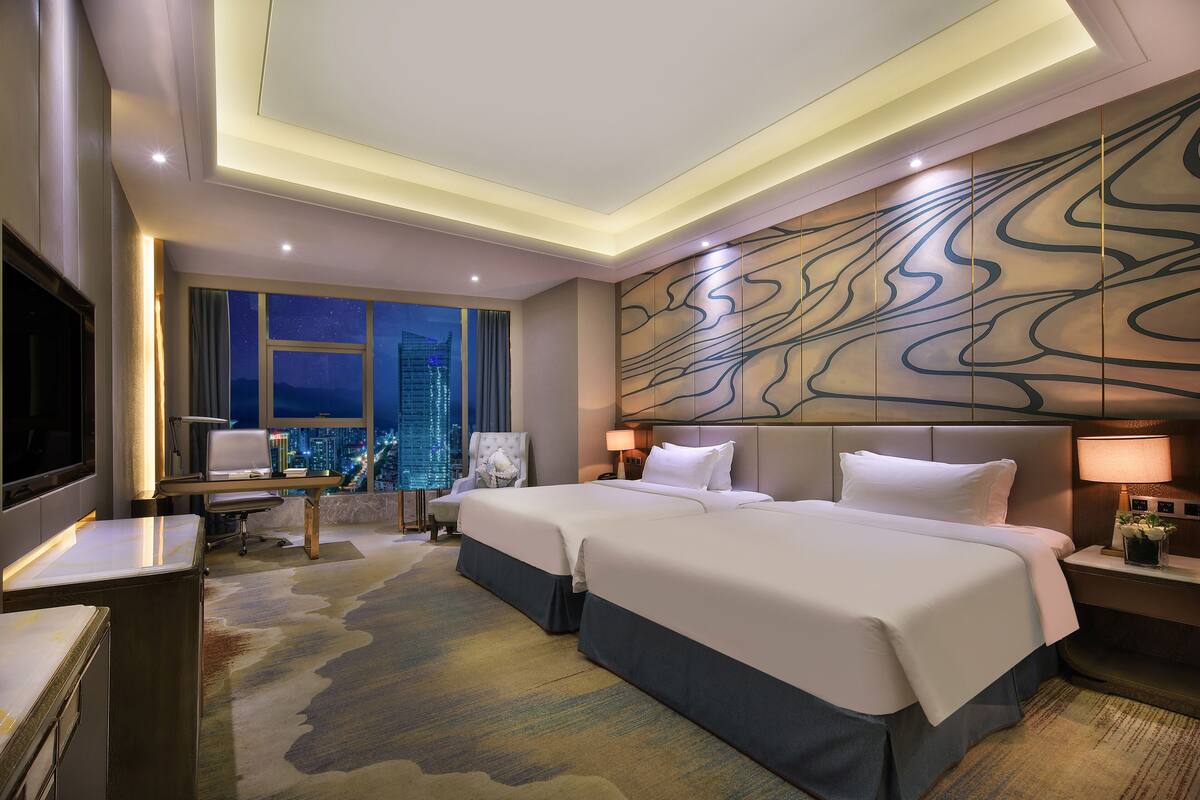 Habitación de hotel con una cama grande, un escritorio, una silla, televisión y vista a la ciudad.