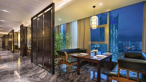 Quarto de hotel moderno com área de refeições, uma janela grande com vista para a cidade e uma planta decorativa.