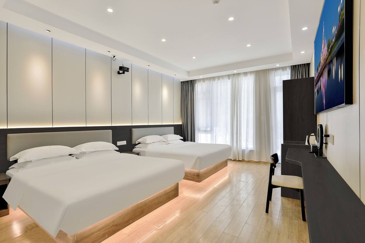 Une chambre d’hôtel avec deux lits, un bureau et un grand téléviseur fixé au mur.