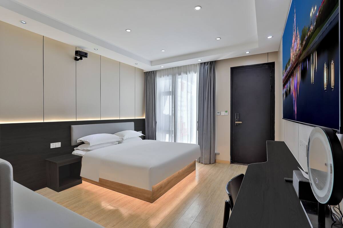 Une chambre d’hôtel moderne avec un grand lit, une table de chevet, un bureau avec un miroir et un téléviseur fixé au mur.