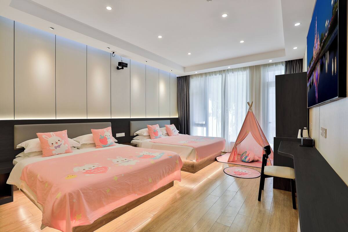Une chambre d’hôtel avec deux lits, une télévision, un bureau et une fenêtre avec des rideaux.