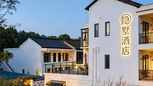 Un hôtel moderne à la façade blanche, doté d’un balcon et d’un espace extérieur bien aménagé avec des sièges, le tout agrémenté d’un éclairage soigné.