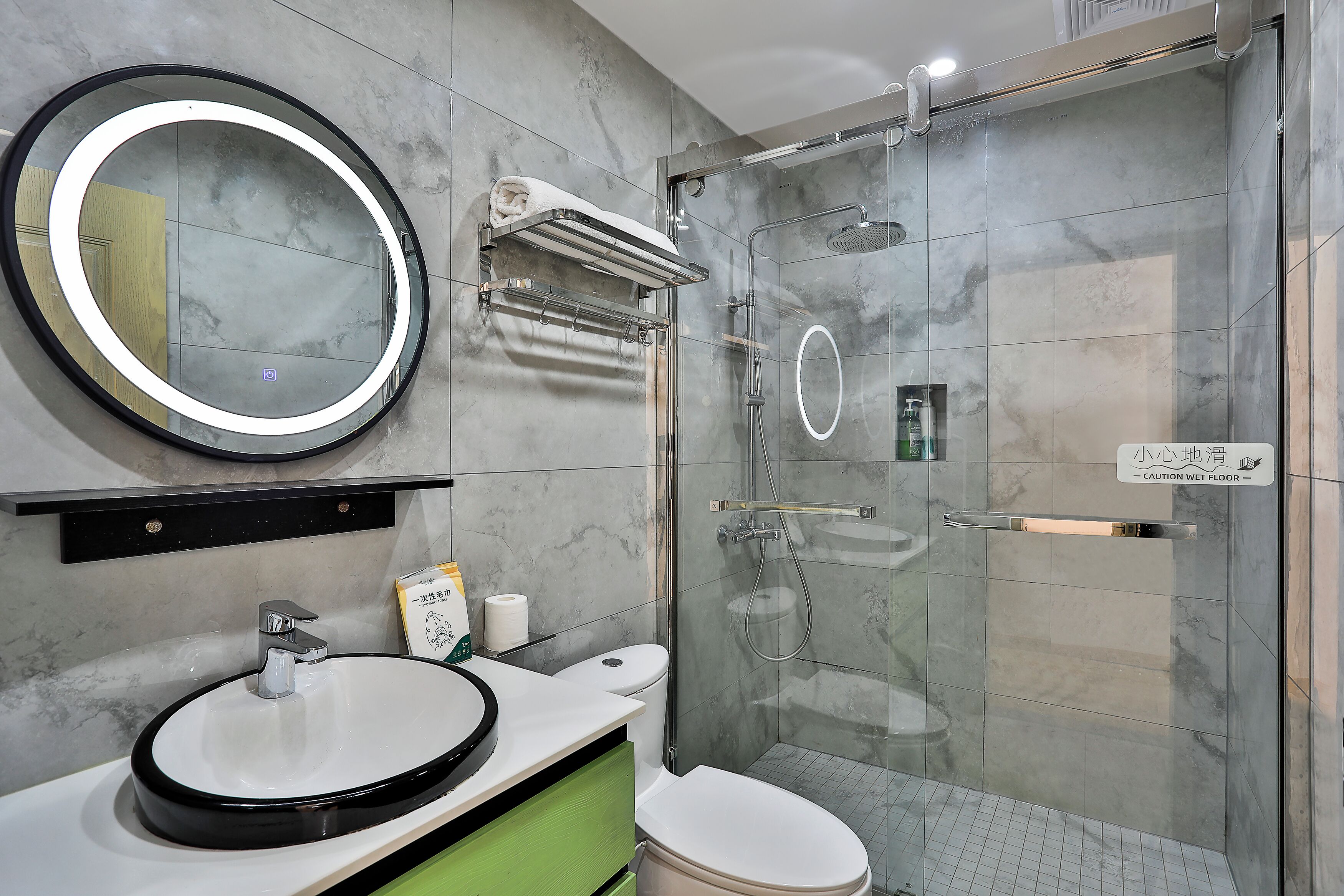 A modern bathroom with a round mirror, a sink, a toilet, and a glass-enclosed shower area.