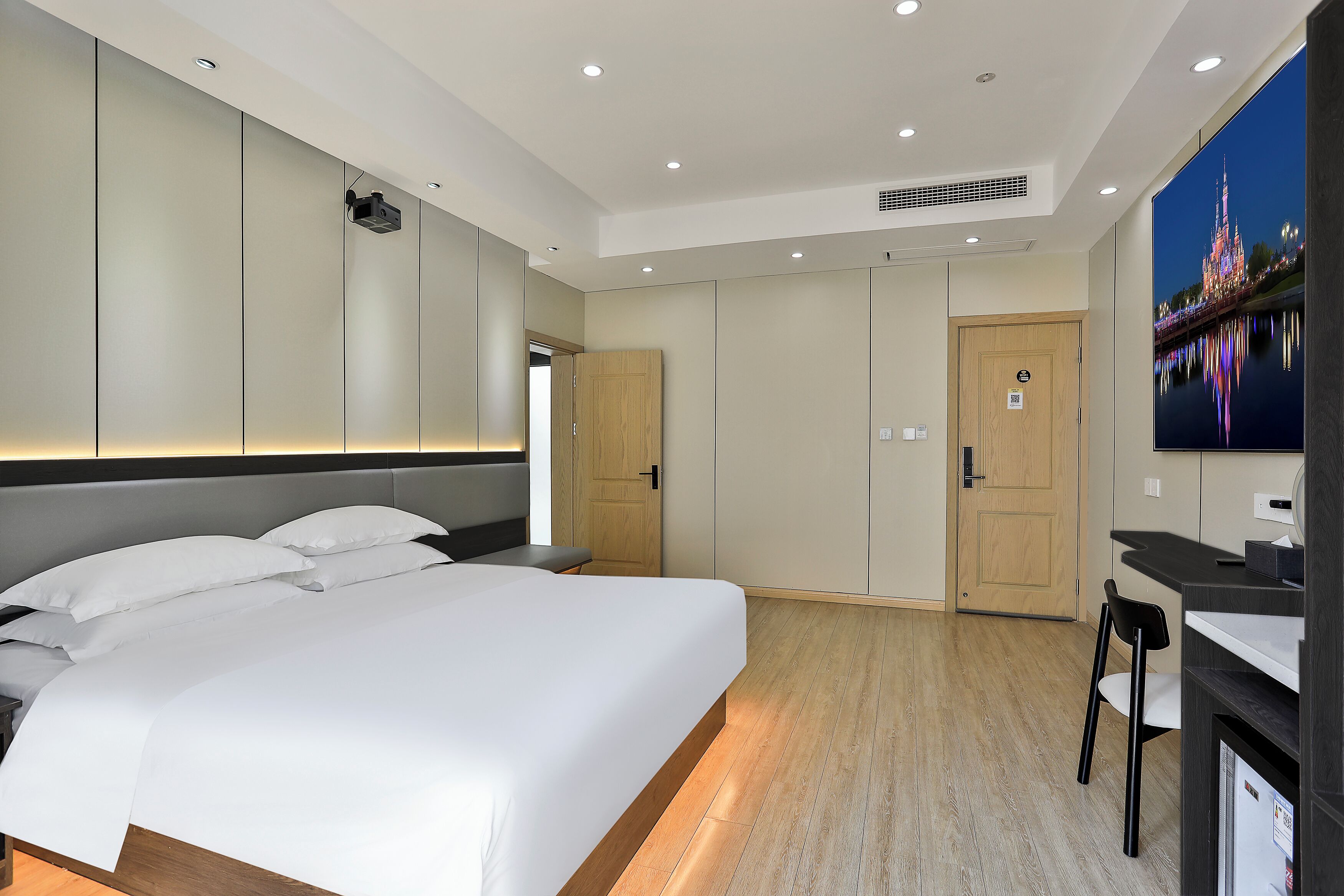 Une chambre d’hôtel moderne avec un grand lit, un bureau et un téléviseur diffusant des images d’un paysage urbain.