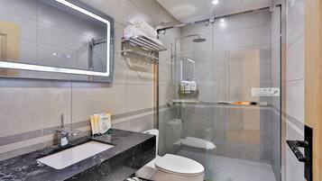 Ein modernes Badezimmer mit einer gläsernen Duschkabine, einer weißen Toilette, einem schwarzen Marmorwaschbecken und einem großen Spiegel.