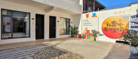A modern building with a flat facade, multiple doors, and a paved entrance area with pebbles.