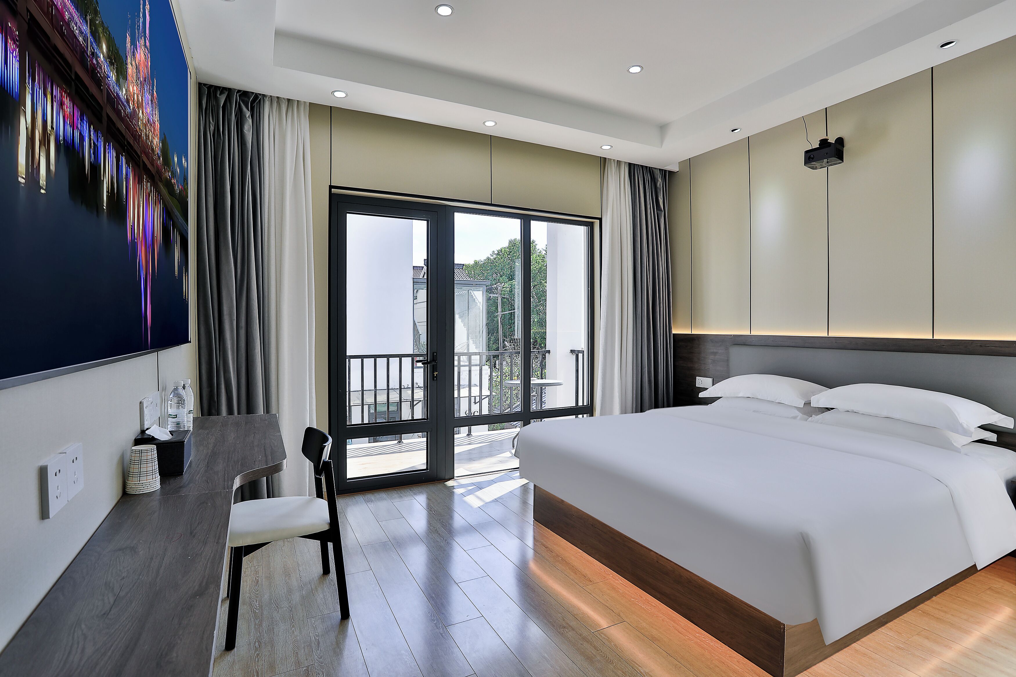 Habitación de hotel moderna con una cama grande, un escritorio y un balcón con vista a la ciudad.