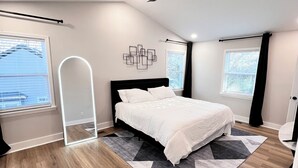 Une chambre à coucher moderne, dotée d’un grand lit, d’un ventilateur de plafond et offrant une vue sur l’extérieur par les fenêtres.