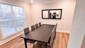 Une salle de conférence avec une longue table, six chaises, un grand miroir et une vue sur la cuisine, visible à travers le miroir.