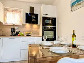Eine moderne Küche mit weißen Schränken, einem Einbauofen, einer Kaffeemaschine und einem Essbereich mit Tellern und Weingläsern.