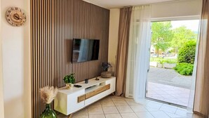 A modern living room with a TV mounted on a wooden panel wall, a white console table, and a green vase with decorative plants. - Apartment Mirta by Interhome (Krk/Šilo)