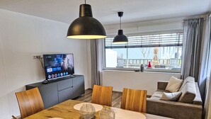 A modern living room with a dining table, wooden chairs, a sofa, and a TV on a cabinet.