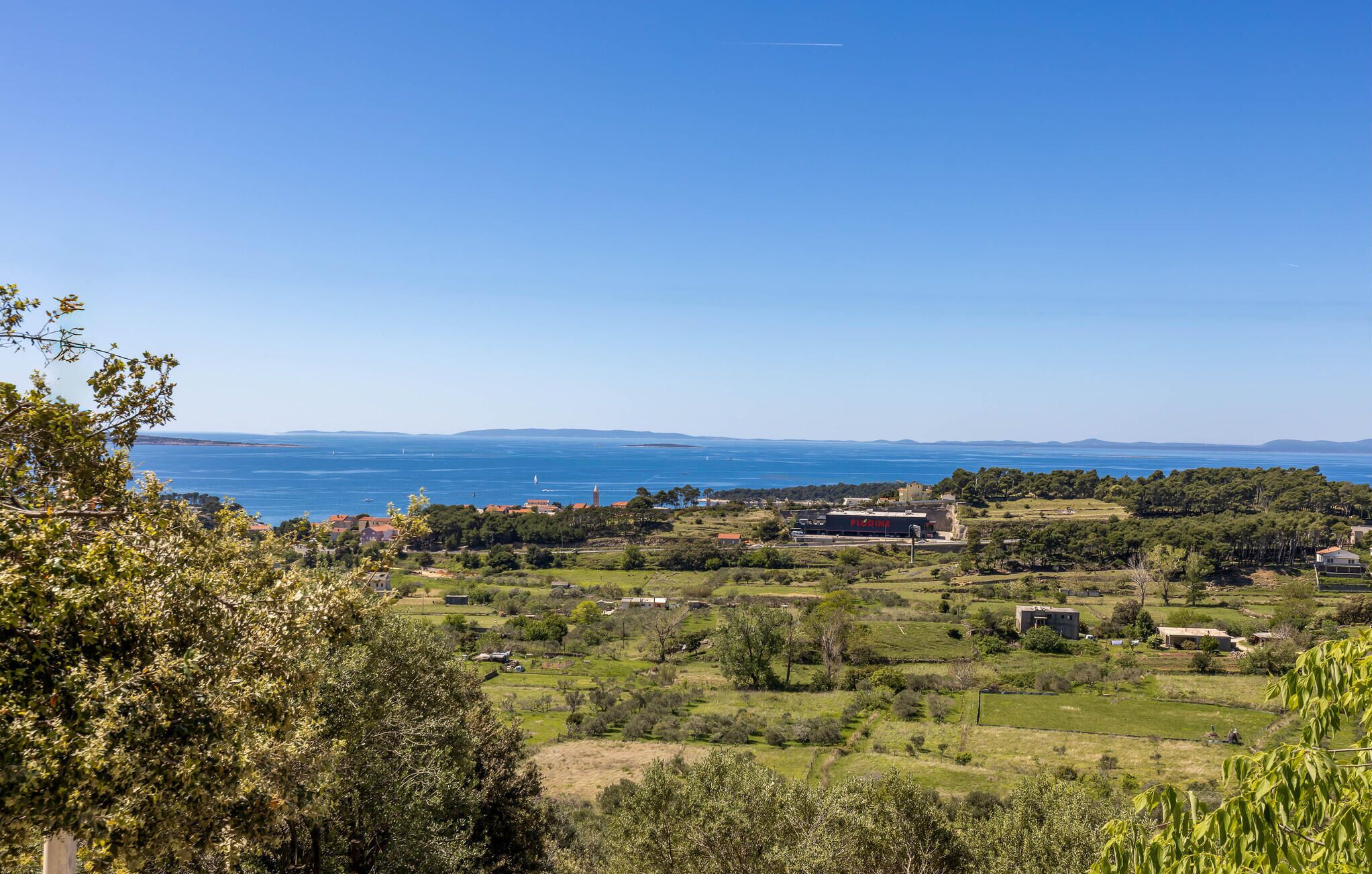 A coastal landscape with buildings, greenery, and a clear view of the sea.