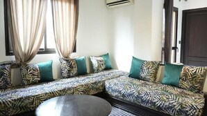 A living room with a sectional sofa, a round coffee table, and a window with curtains. - Bayt al atlas (Marrakech)