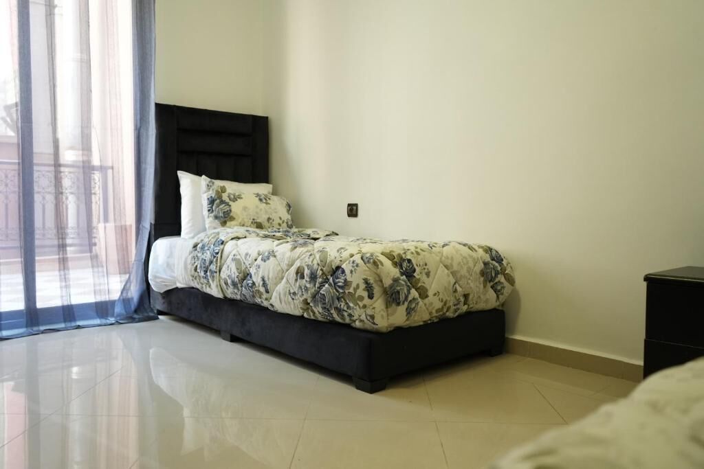 A bedroom with a bed, a nightstand, and a window with sheer curtains.