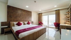 Una habitación de hotel moderna con una cama grande, dos sillas rojas, un escritorio y un balcón con vistas.